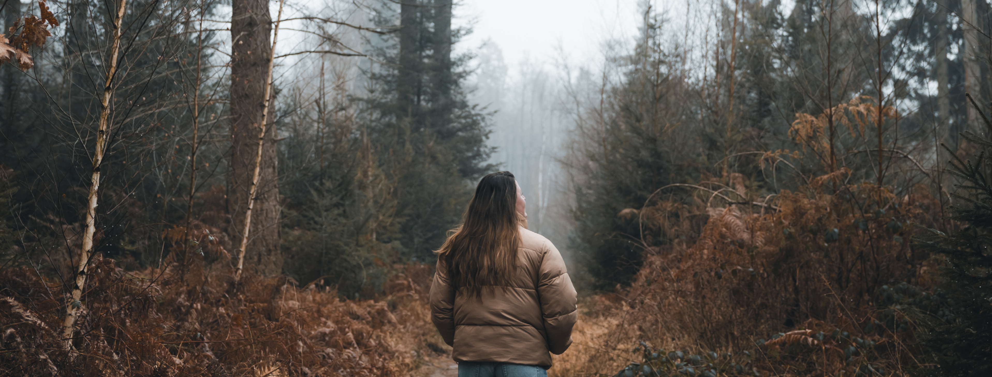 Persoon met lange haren loopt over een smal bospad in een mistig naaldbos in de Meinweg.