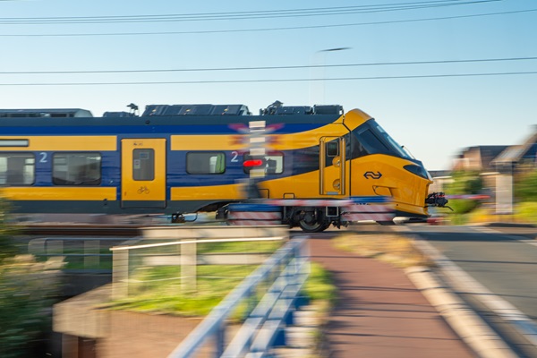 De nieuwe trein van de NS, de ICNG, raast voor bij een spoorwegovergang waar de lichten rood flikkeren