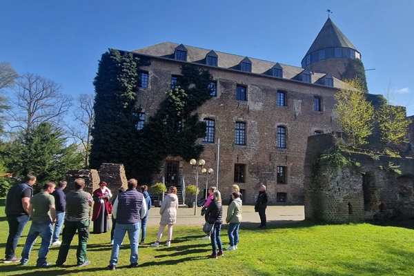 Tour of Brüggen Castle with a guide in period clothing and a group of visitors on a sunny day.