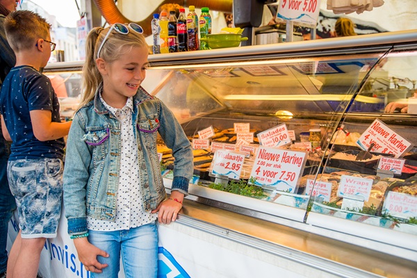 Ein lächelndes Mädchen an einem Fischstand auf einem Markt in Weert, mit Heringen und anderen frischen Meeresfrüchten in der Vitrine.