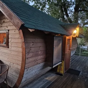 Houten tonvormige overnachtingscabine op een houten vlonder, sfeervol verlicht in de schemering, omringd door bomen bij Simonshoek.